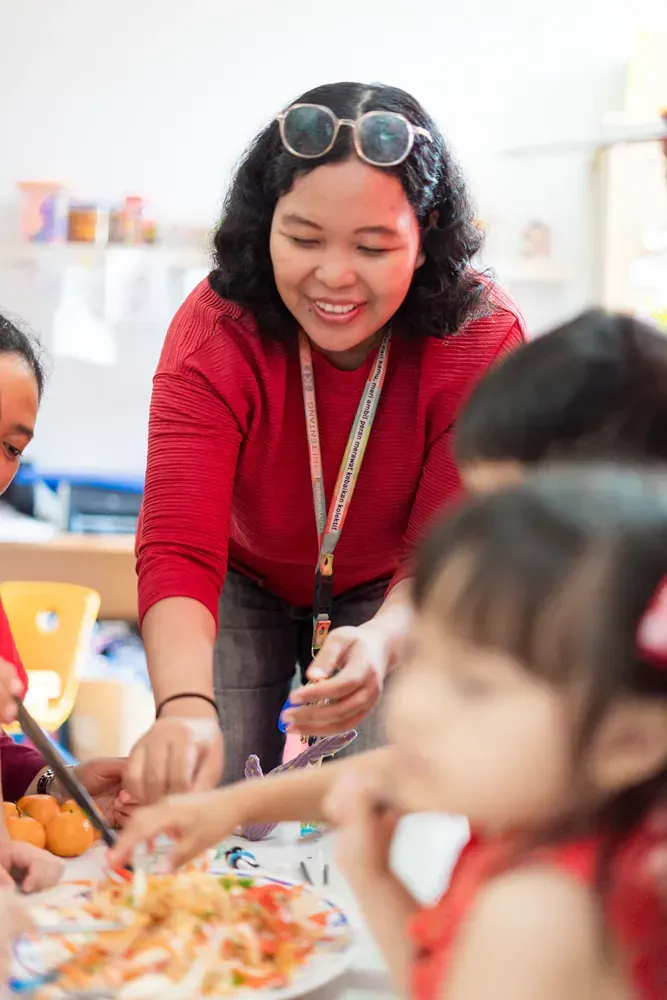 A woman is teaching a group of children how to eat food in a classroom.