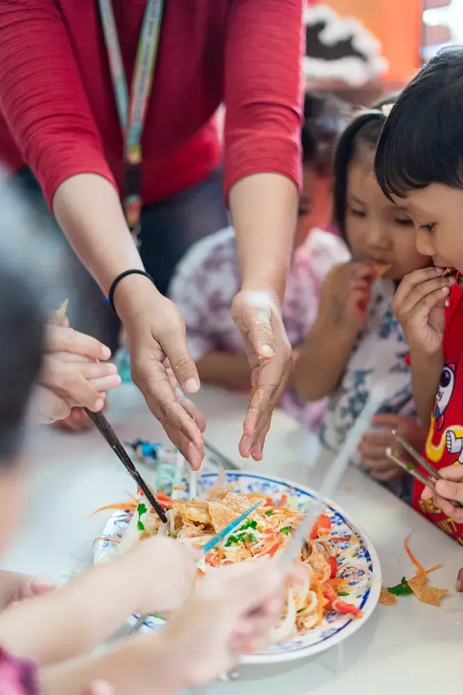 A group of children are sitting at a table eating food with chopsticks.