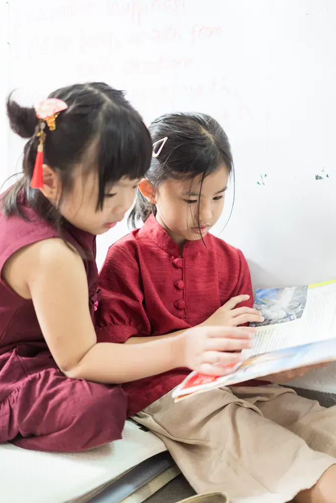 Two little girls are sitting next to each other reading a book.