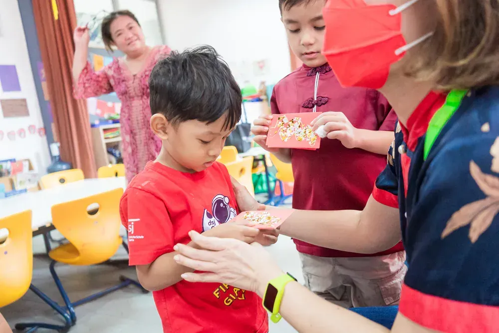 A woman is giving a gift to a young boy in a classroom.