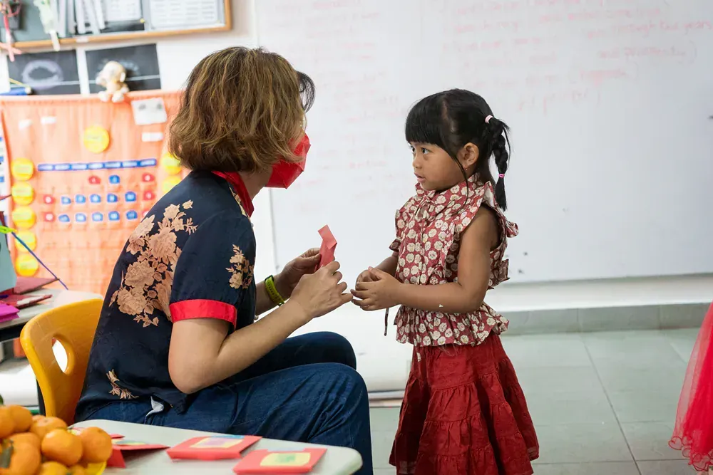 A woman is sitting at a table talking to a little girl.