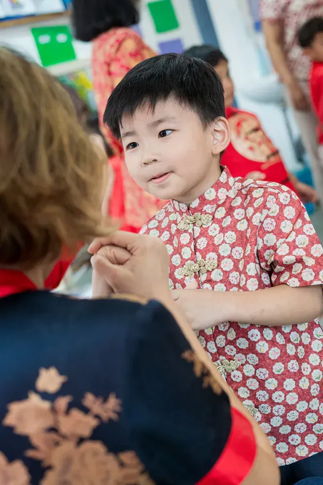 A young boy is holding hands with a woman in a classroom.