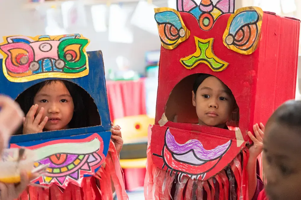 Two young girls are wearing cardboard dragon costumes.