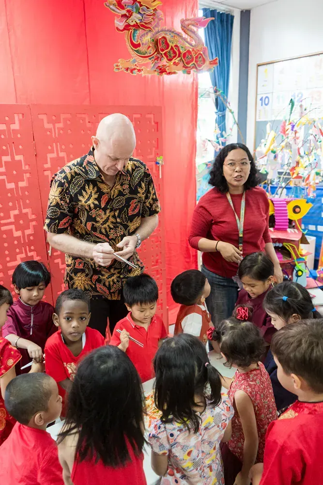 A man and woman are standing in front of a group of children in a classroom.