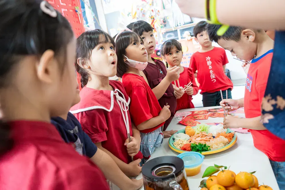 A group of children are standing around a table eating food.