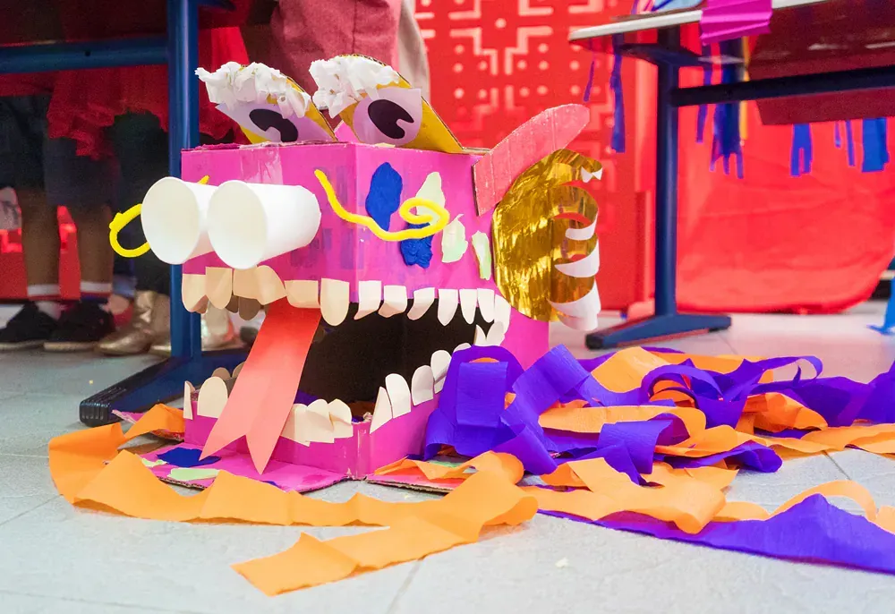 A dragon made out of cardboard and paper is sitting on the floor.
