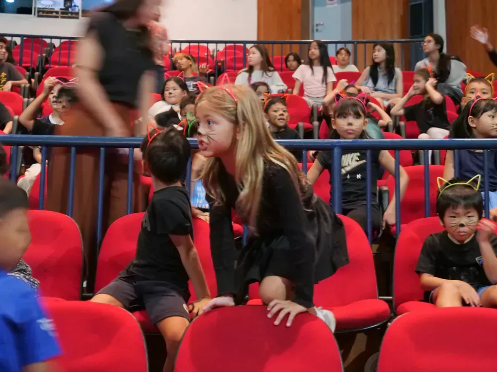A group of children are sitting in red chairs in a theater.