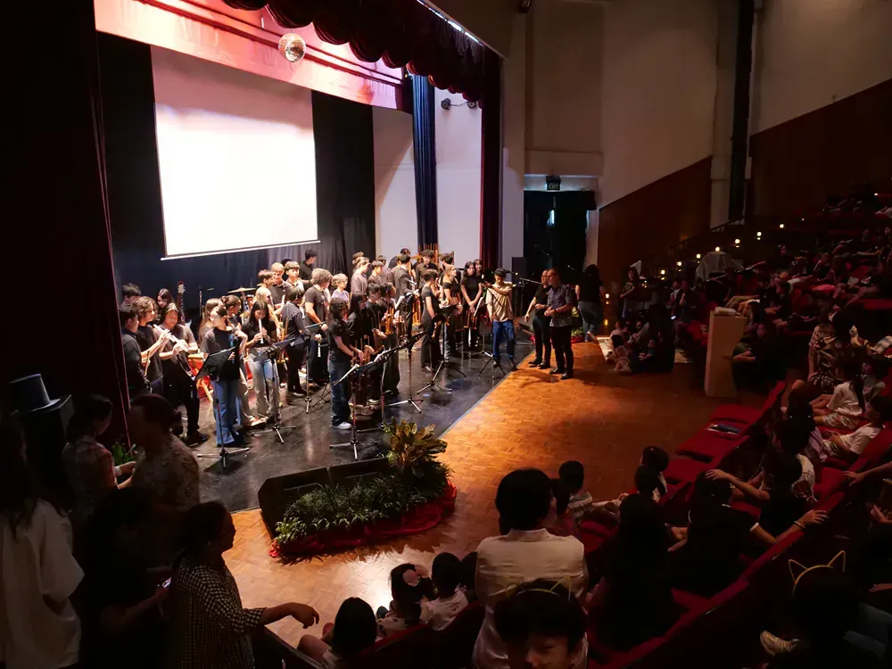 A large group of people are sitting in an auditorium watching a band perform on stage.