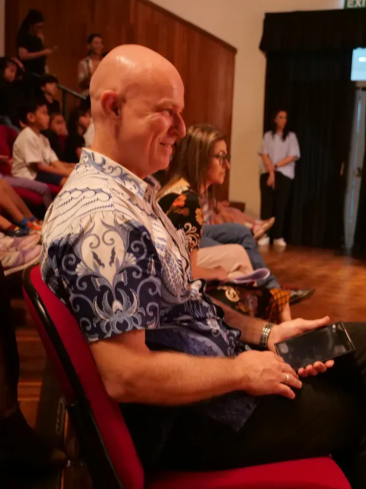 A bald man in a blue and white shirt is sitting in a red chair.