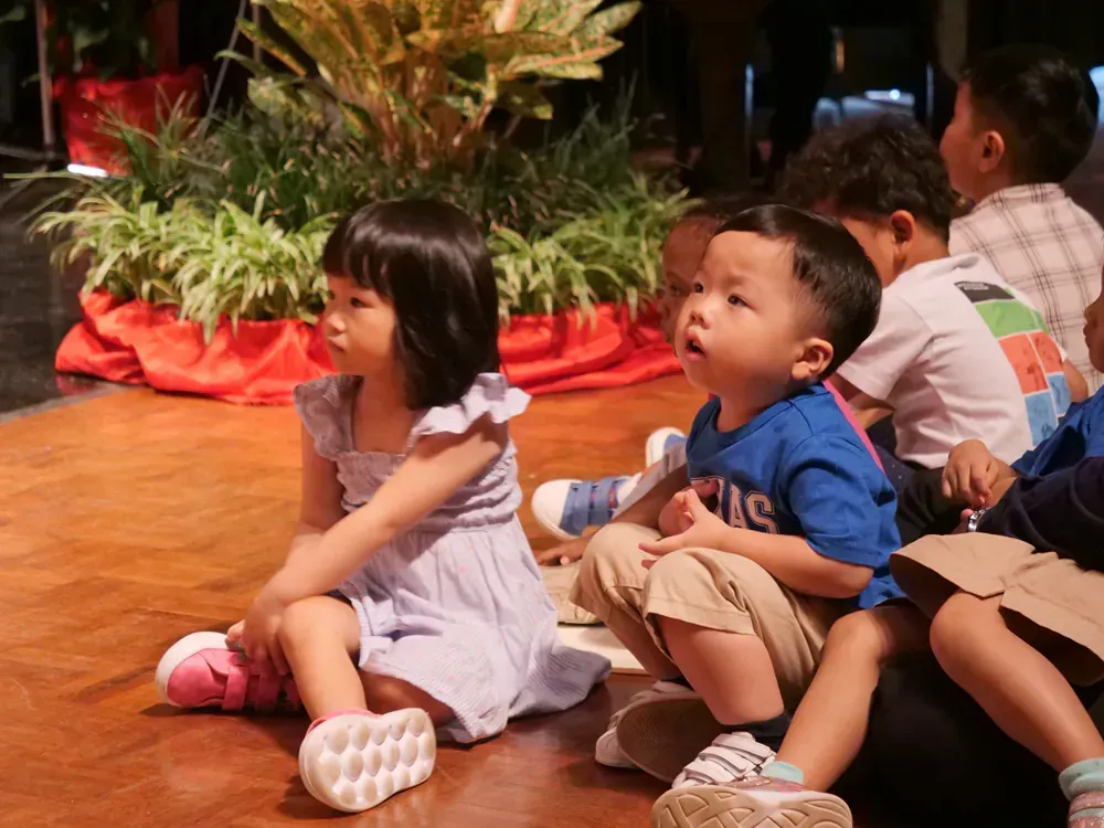 A group of children are sitting on the floor and one of them is wearing a shirt that says kings