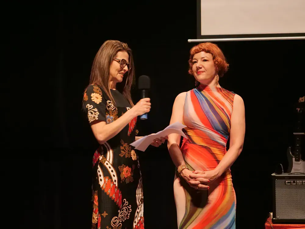Two women are standing on a stage and one is holding a microphone