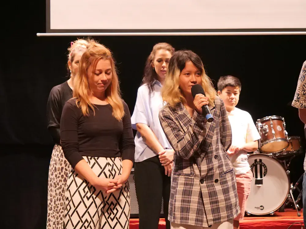 A woman is holding a microphone in front of a group of people on a stage.