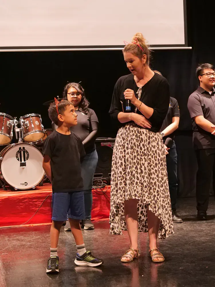 A woman is speaking into a microphone while standing next to a young boy on a stage.