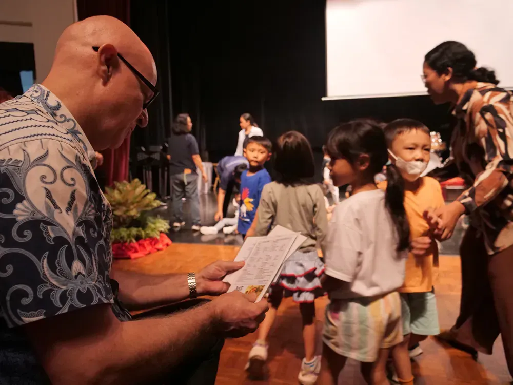 A group of children are standing around a man holding a piece of paper