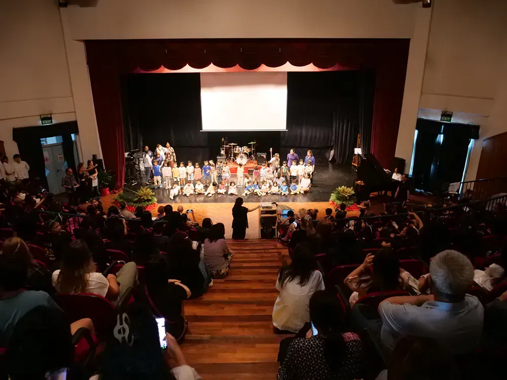 A large group of people are sitting in an auditorium watching a concert.
