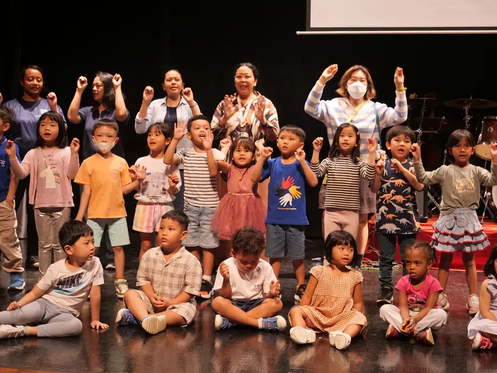 A group of children are sitting on the floor on a stage.