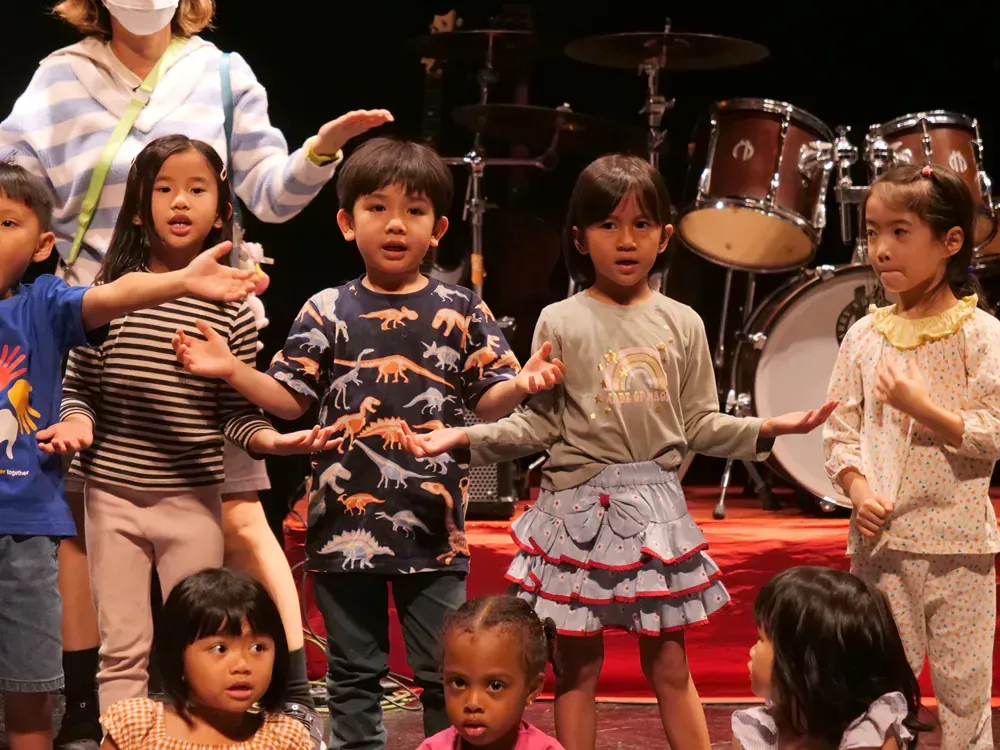 A group of children are standing on a stage in front of a drum set.