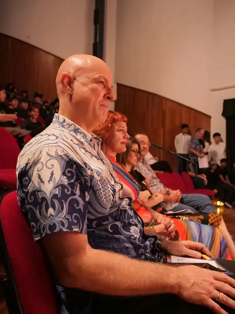 A group of people are sitting in red chairs in an auditorium.
