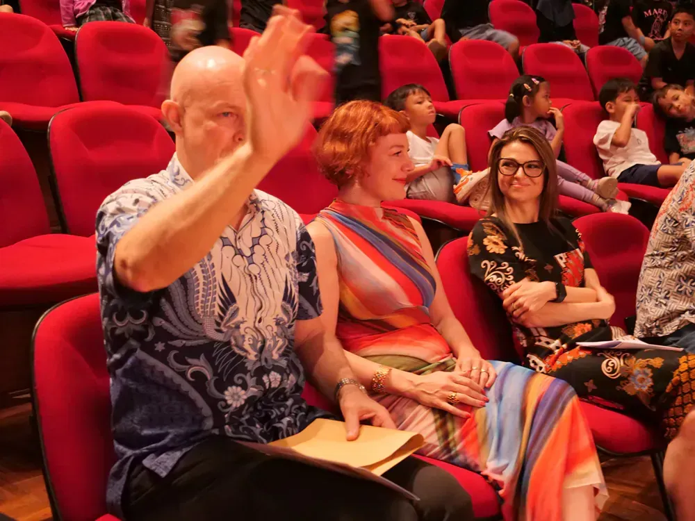 A group of people are sitting in red chairs in an auditorium.