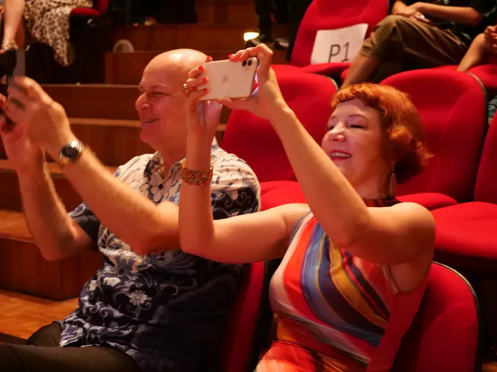 A man and a woman are taking a selfie in an auditorium with a sign that says p1
