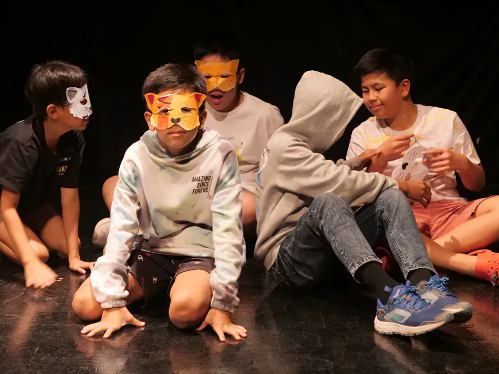 A group of children wearing masks are sitting on the floor.