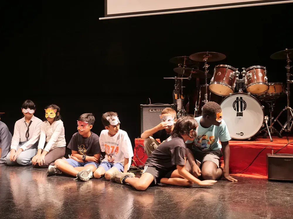 A group of children are sitting on the floor in front of a drum set.