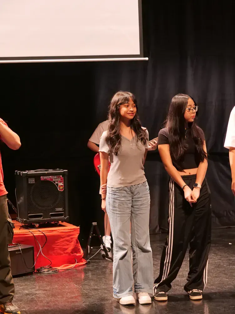 A group of people are standing on a stage in front of a projector screen.