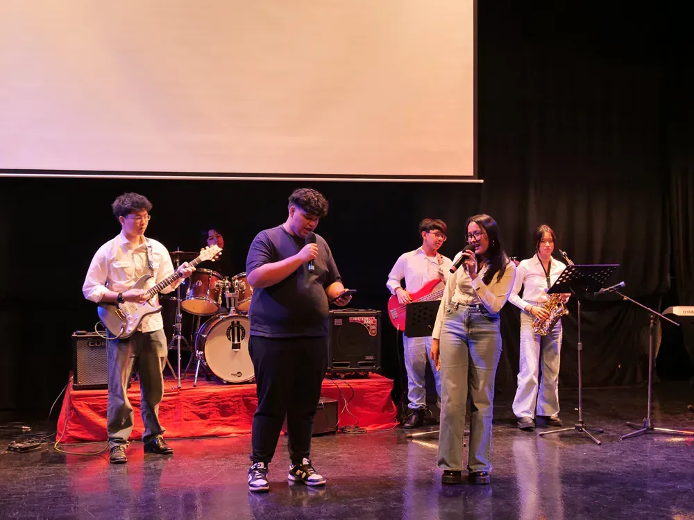 A group of people are standing on a stage playing instruments and singing into microphones.