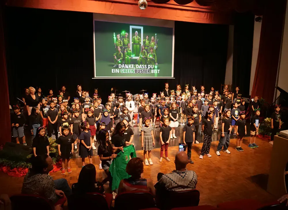 A large group of children are standing on a stage in front of a large screen.