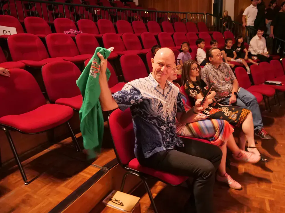 A group of people are sitting in red chairs in an auditorium.