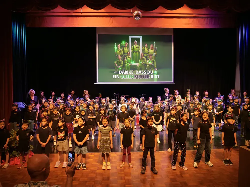 A large group of children are standing on a stage in front of a large screen.