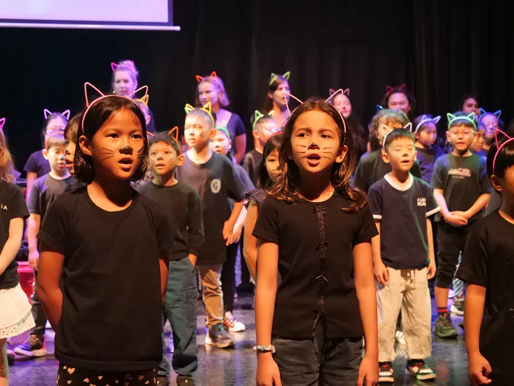 A group of children wearing cat ears are singing on a stage.
