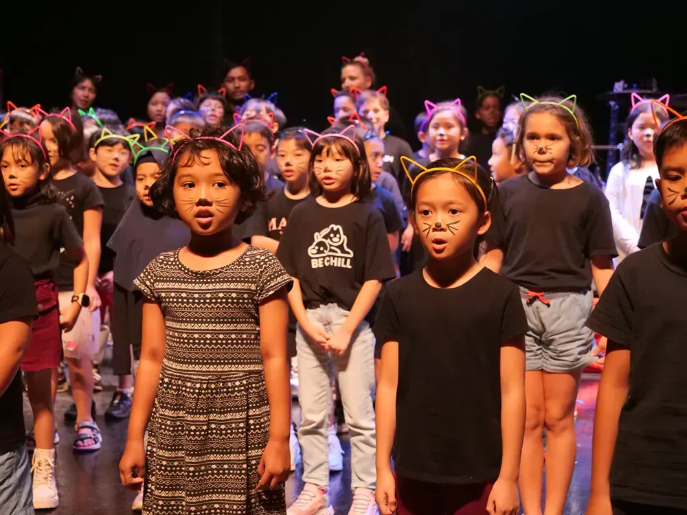 A group of children wearing cat ears are singing on a stage.