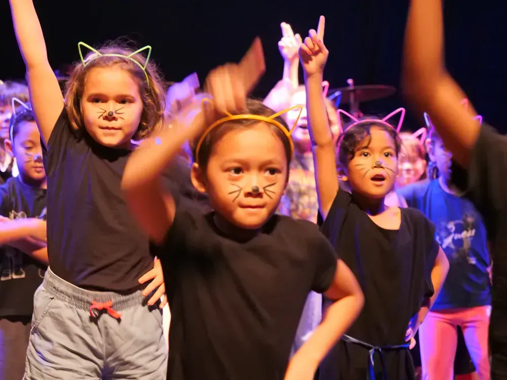 A group of young girls wearing cat ears are dancing on a stage.