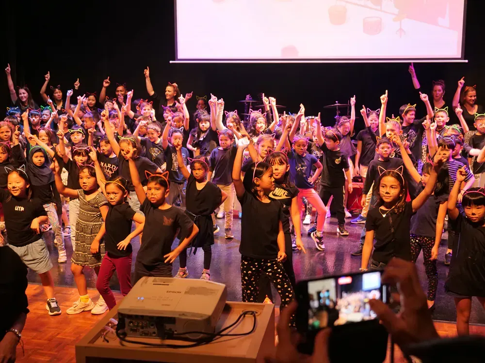 A group of children are dancing on a stage in front of a projector.
