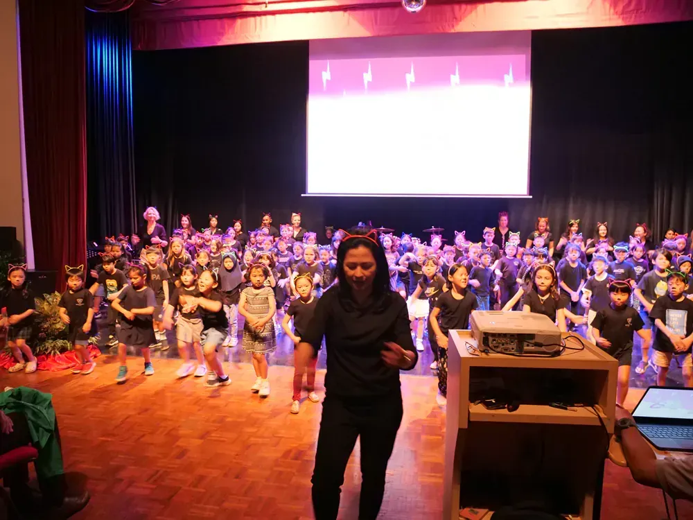 A woman is standing in front of a large group of children on a stage.