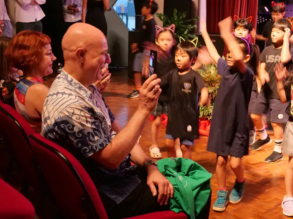 A man is sitting in a theatre watching a group of children dancing.