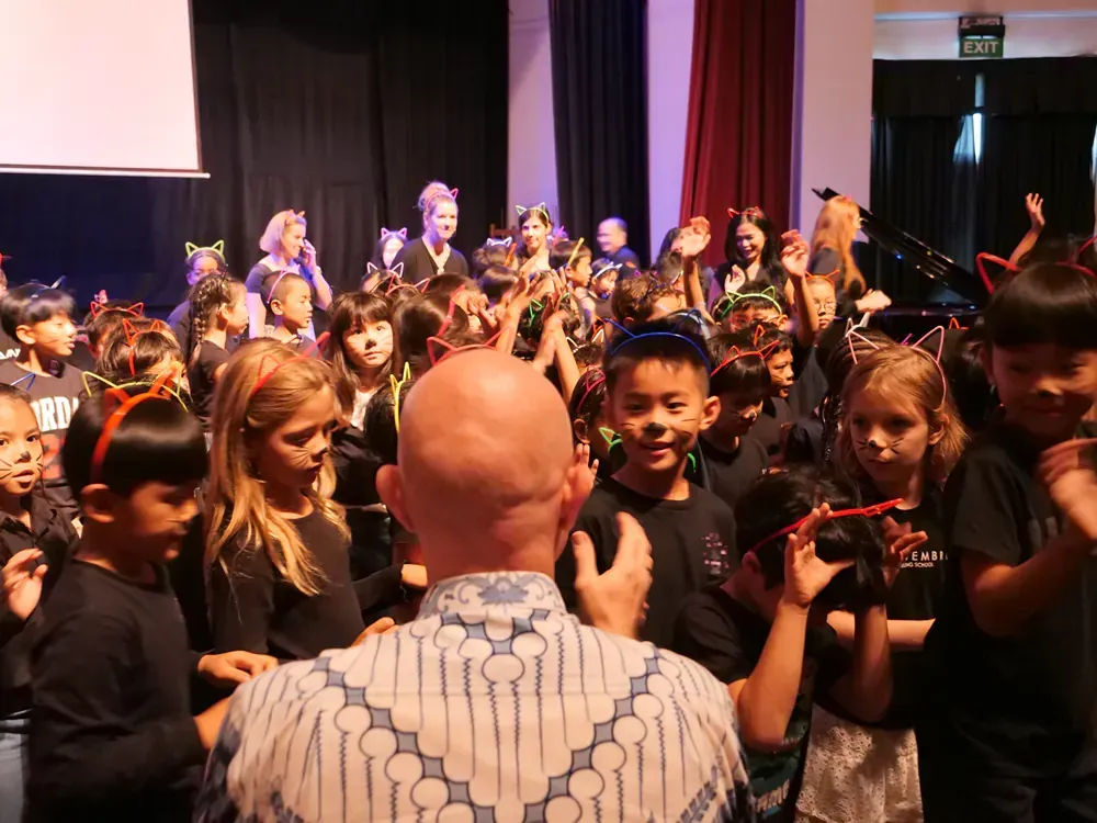 A bald man is standing in front of a crowd of children.
