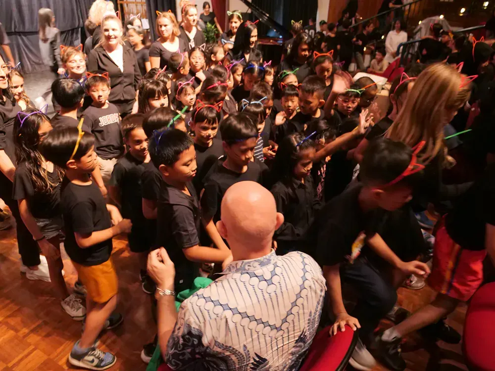 A bald man is sitting in front of a crowd of children