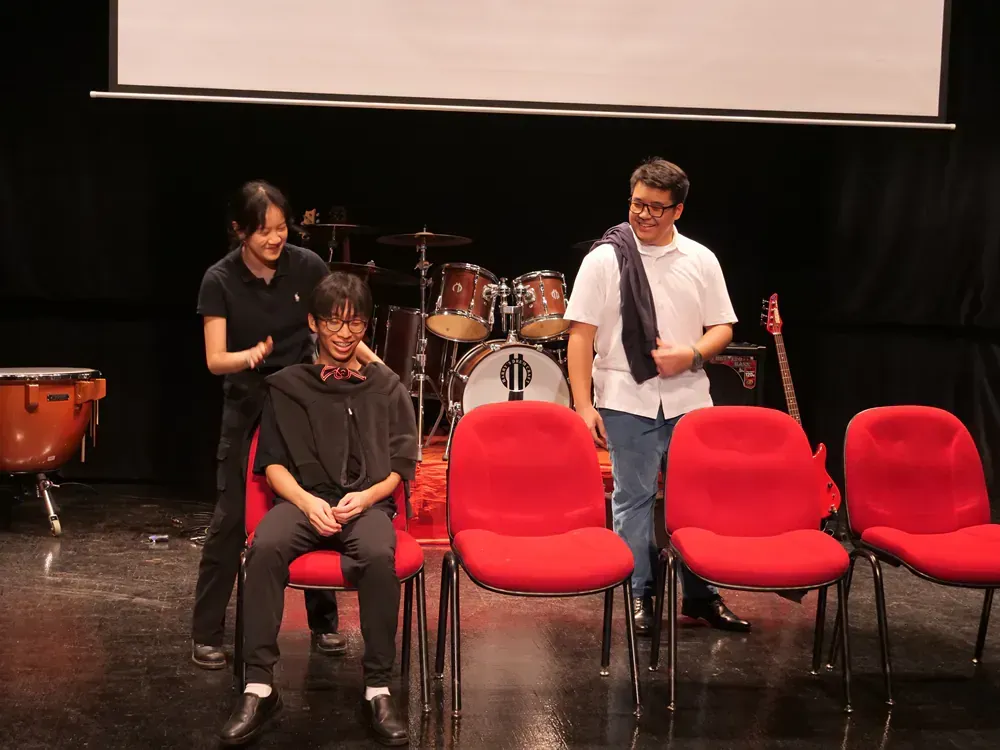 A group of people are sitting in red chairs on a stage in front of a drum set.