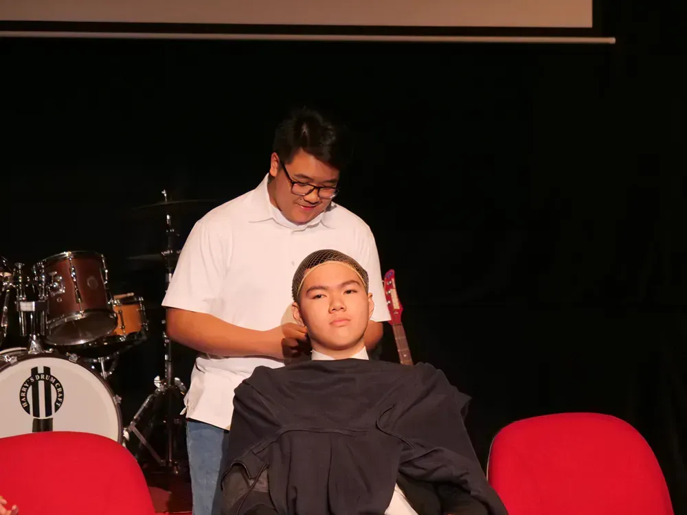 A man in a black cloth sitting while another man is standing behind him