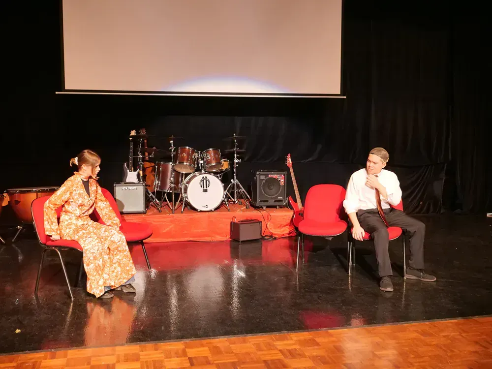 A man and a woman are sitting on a stage in front of a drum set