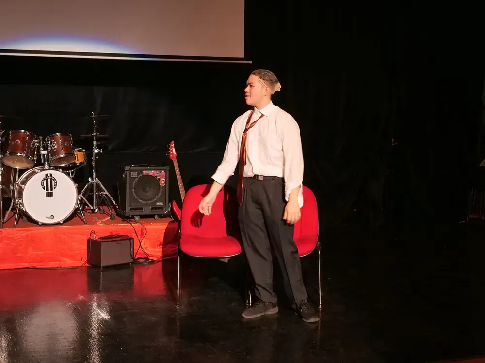 A man in a white shirt and tie is standing in front of a drum set