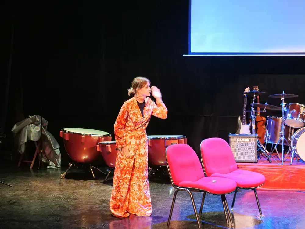 A woman is singing into a microphone on a stage in front of a drum set.
