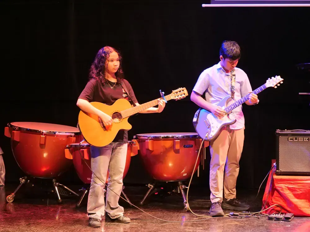 A man and a woman are playing guitars and drums on a stage.