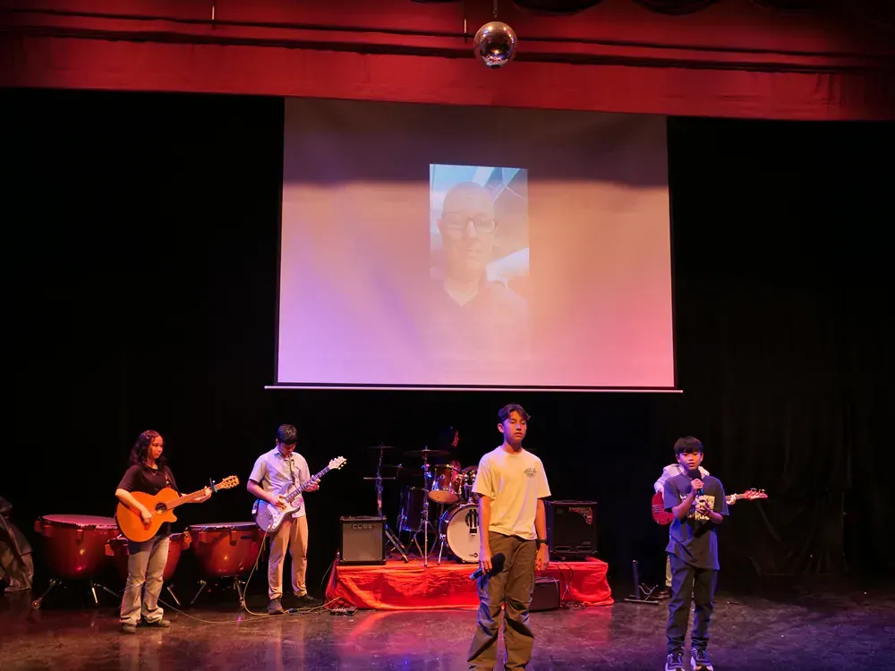 A group of young men are playing instruments on a stage in front of a large screen.