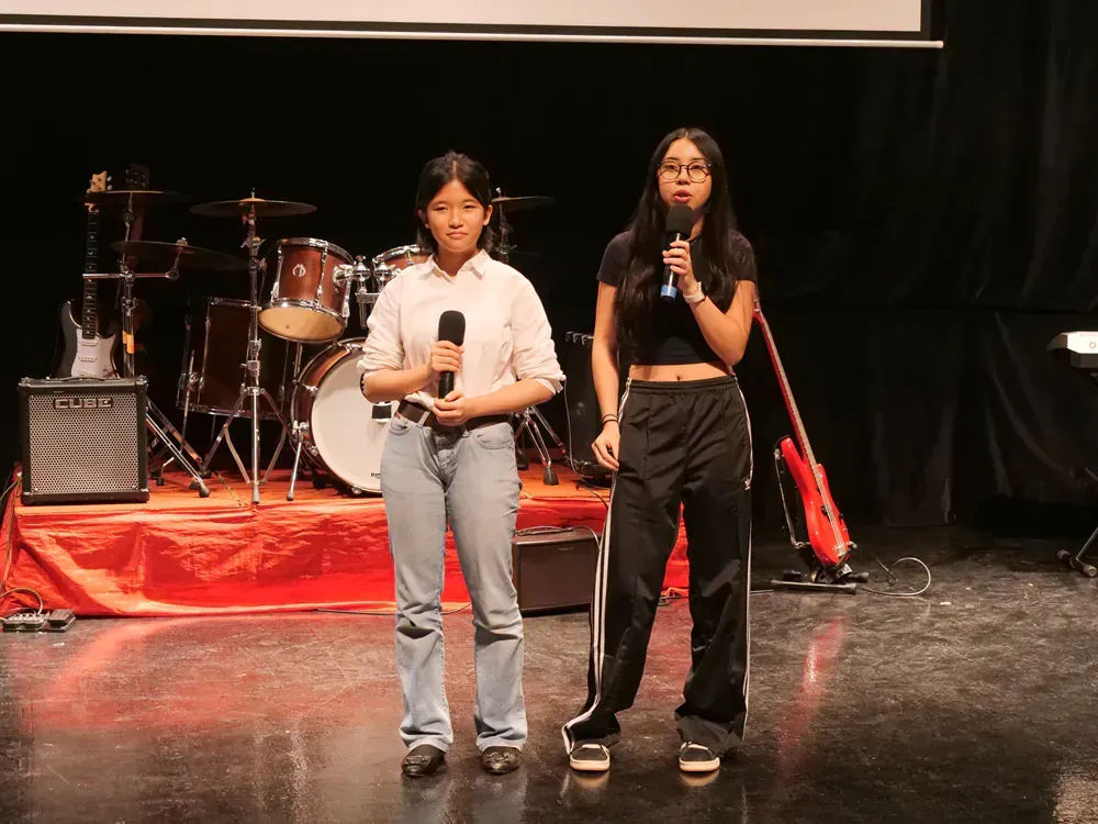 Two girls are standing on a stage holding microphones.