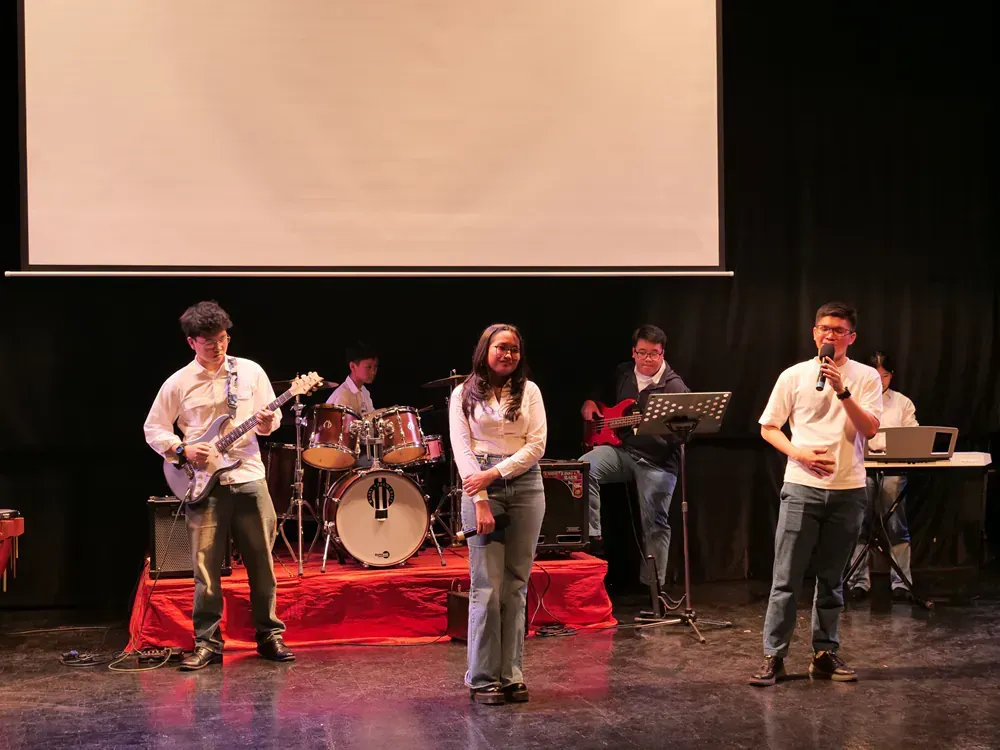 A group of people are standing on a stage playing instruments and singing into microphones.