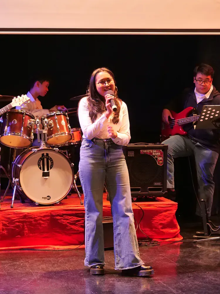 A woman is singing into a microphone in front of a drum set.