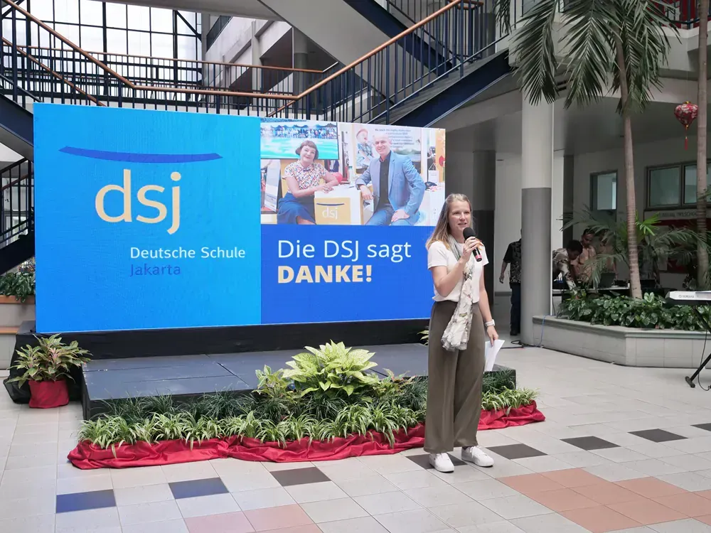 A woman is standing in front of a large screen that says dsj